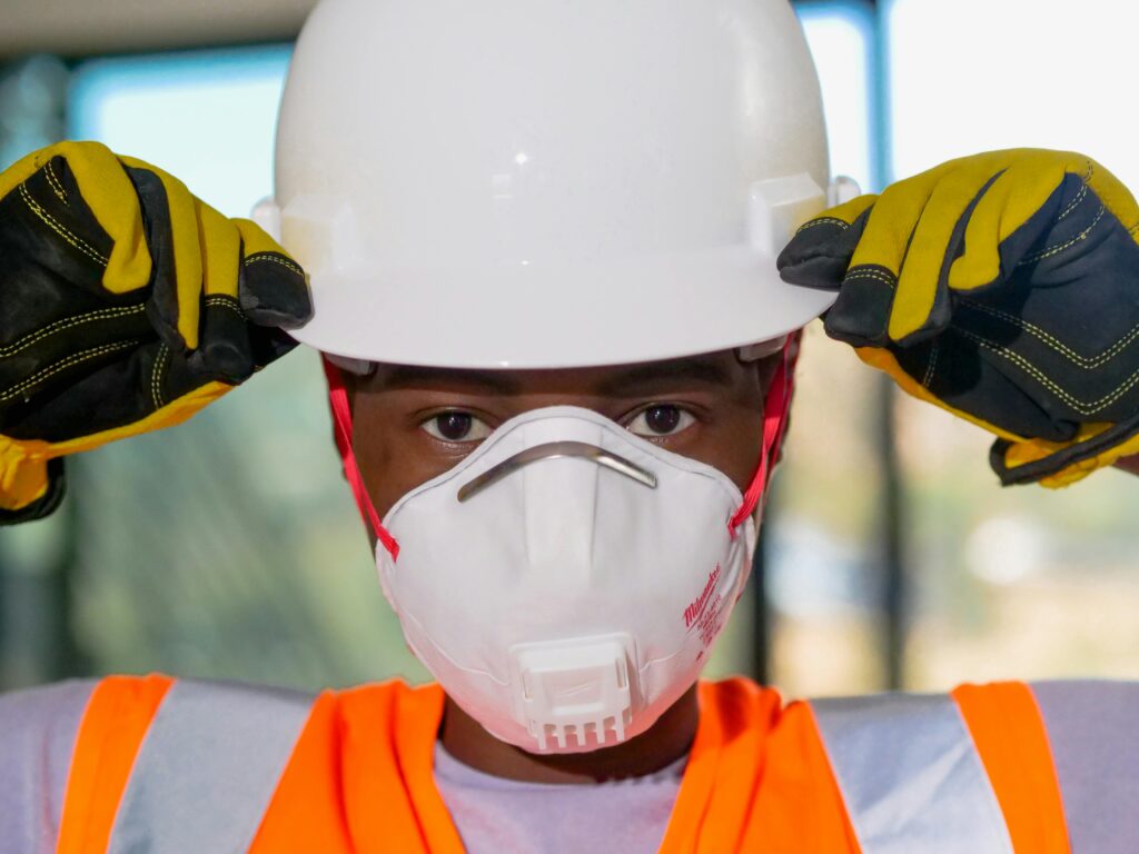 Close-up of a construction worker wearing safety gear including a hardhat, N95 mask, and gloves.